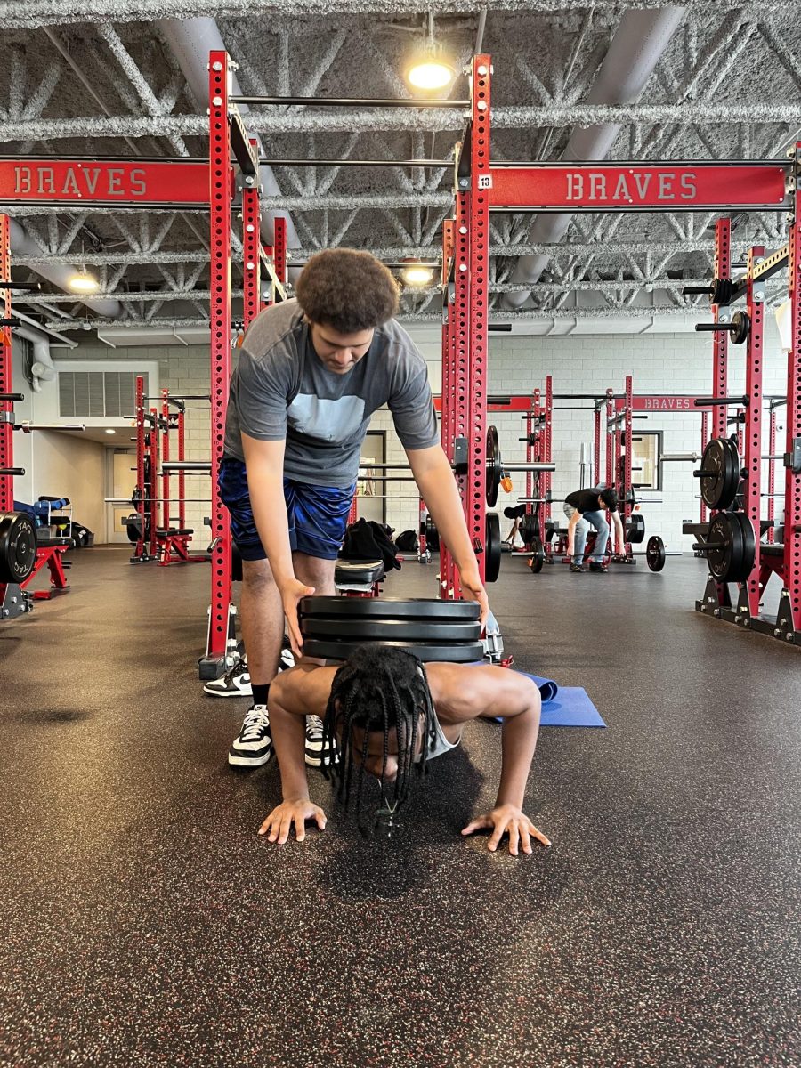 Freshman Jaylyn Clark works with junior Jacob Klomp to perform a weighted push up in the Bremen weight room after school May 5. Clark managed to do multiple weighted pushups with the help of Klomp!